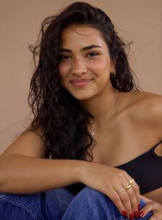 Woman with long wavy hair and freckles wearing a black top and jeans