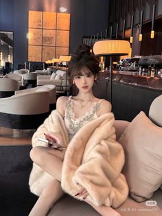 Woman in a fur coat and lace top sitting on a sofa indoors