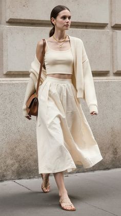 Woman in a cream crop top, midi skirt, and cardigan walking outdoors