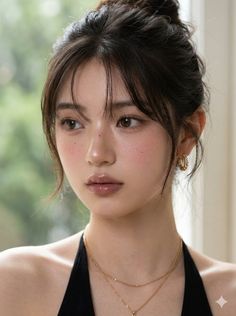Woman with dark hair in an updo, wearing a black top and gold jewelry