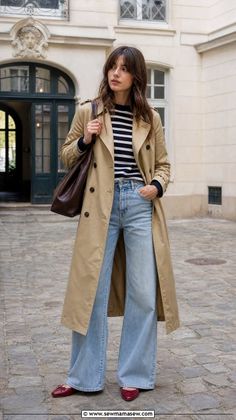 Woman in a trench coat, striped shirt, and wide leg jeans on a cobblestone street