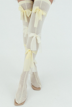 Legs wearing sheer thigh-high stockings with yellow bows and square-toe shoes