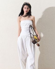 Woman in a white strapless top and pants holding a small handbag