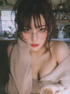 Woman with messy hair and glasses wearing an off-shoulder sweater indoors