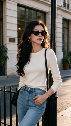 Woman with long dark hair and sunglasses leaning against a pole at golden hour