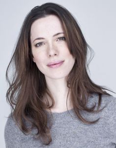 Woman with long brown hair wearing a grey sweater, looking at the camera