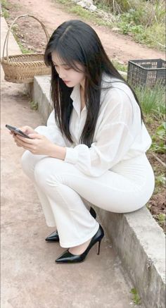 Woman with long black hair in a white outfit and black heels, squatting outdoors