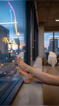 Bare feet with red nail polish and an anklet resting on a ledge overlooking a city at night