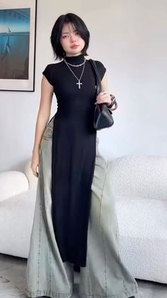 Woman in a black dress with wide leg pants and a cross necklace indoors