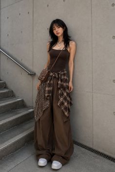 Woman in a brown tank top and baggy pants with a plaid shirt tied around her waist