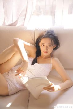 Woman in a white top and shorts reading a book on a couch