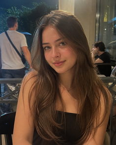 Young woman with long brown hair wearing a black top indoors at night