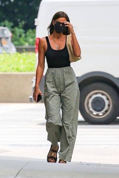Woman in a black tank top, cargo pants, and face mask walking outdoors