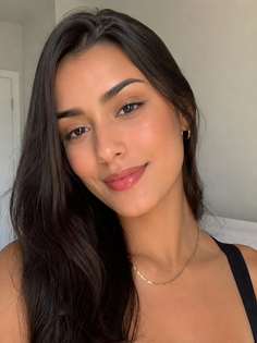 Woman with long dark hair and gold jewelry smiling at the camera