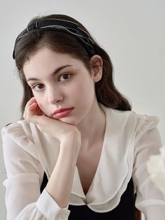Woman with long hair and a black headband wearing a white blouse