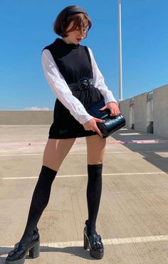 Woman in a black dress and white shirt with knee high socks and platform shoes