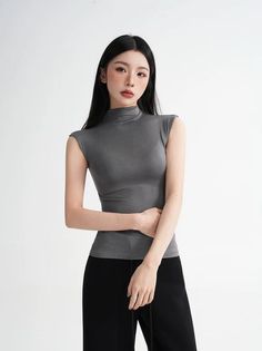 Woman with long black hair wearing a gray top and black pants in a studio