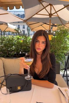 Woman with long dark hair holding a cocktail at an outdoor cafe