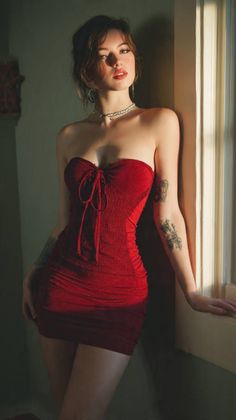 Woman in a red strapless dress with tattoos, leaning against a wall
