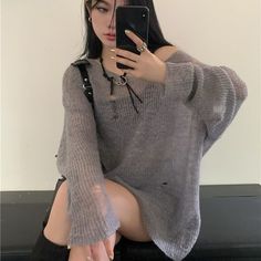 Woman in a distressed gray sweater taking a selfie indoors