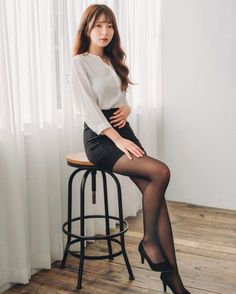 Woman with long hair in a white shirt and black skirt sitting on a stool