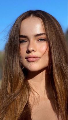 Close-up portrait of a woman with long brown hair and blue eyes outdoors