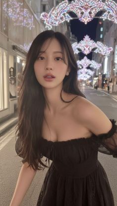 Woman in a black off-shoulder dress on a street at night with decorative lights