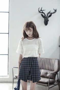 Woman with long hair wearing a plaid skirt and white t-shirt indoors