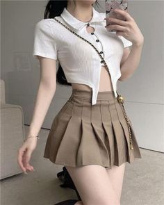 Woman in a white crop top and brown pleated skirt taking a mirror selfie