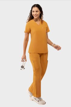 Woman in mustard yellow scrubs holding a stethoscope and smiling