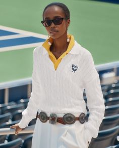 Woman in sunglasses and a white sweater with a concho belt on a tennis court