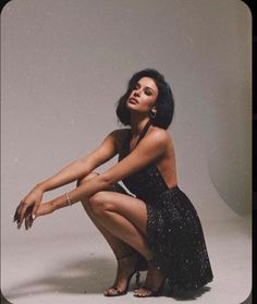 Woman in a black dress and high heels squatting in a studio