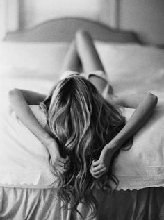 Woman with long wavy hair lying on a bed in black and white
