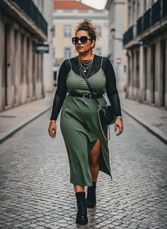 Woman in a green slip dress and black boots walking on a cobblestone street