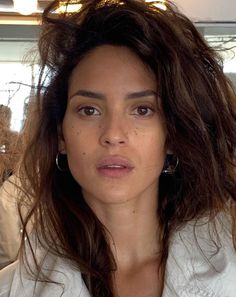 Woman with long brown hair and freckles wearing a white shirt and hoop earrings