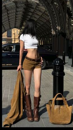 Woman in a white crop top and brown shorts with a jacket and bag on a street