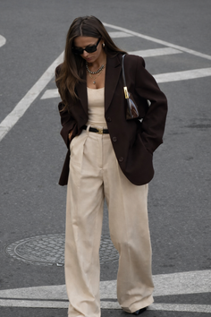Woman in a brown blazer and wide leg pants standing on a street