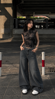 Woman in a sheer dragon-patterned top and wide-leg jeans in an urban setting