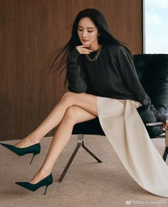 Woman with long dark hair wearing a sweater and high heels, sitting indoors