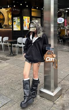 Person in a black hoodie and camo hat with platform boots on a city street