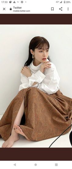 Woman with long hair wearing a white shirt and brown skirt, sitting indoors