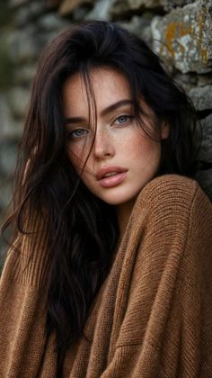 Woman with long dark hair and freckles wearing a brown sweater outdoors