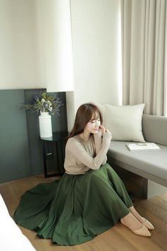 Woman with long hair wearing a green skirt and beige top, sitting indoors
