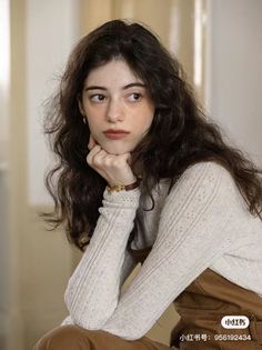 Woman with long wavy hair and freckles wearing a light sweater and brown overalls