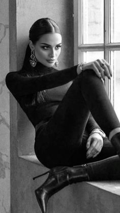 Woman in a black turtleneck and high heels sitting by a window