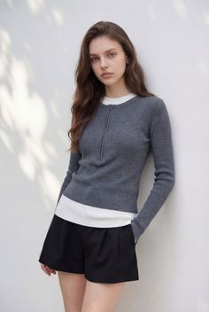 Woman with long hair wearing a gray sweater and black shorts outdoors