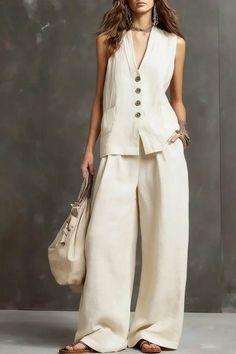 Woman in a cream sleeveless top and wide leg pants holding a bag