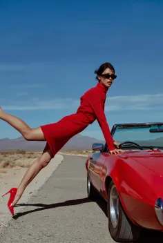 Woman in a red dress and high heels posing with a red convertible on a desert road