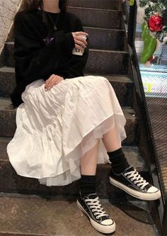 Person in a black sweatshirt and white skirt sitting on stairs