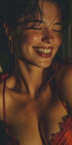 Woman in red lingerie with closed eyes and a smile, illuminated by soft light